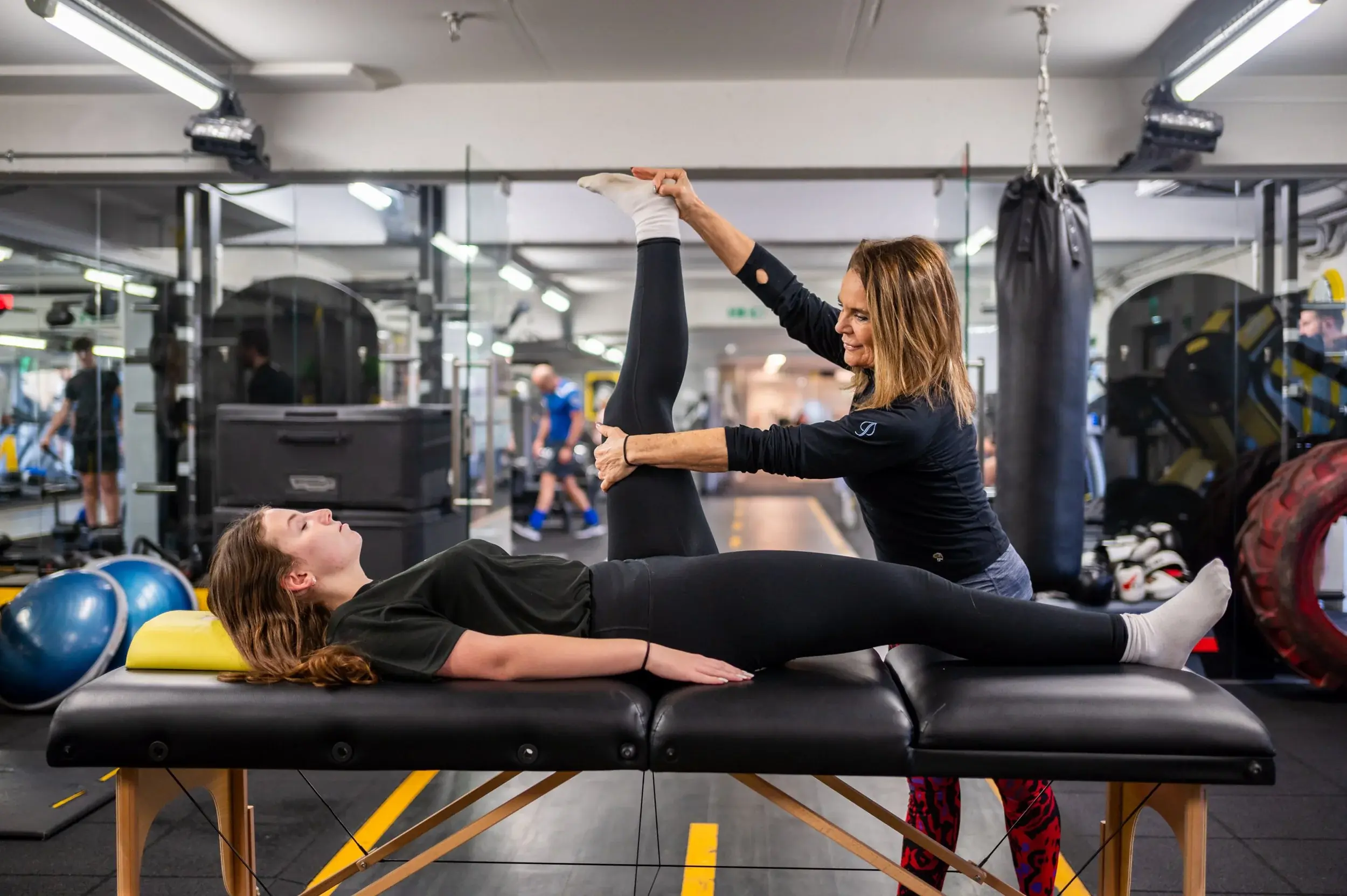 A trainer stretching a client on the gym floor